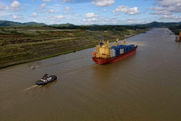 shutterstock_2480136187 A cargo ship being assisted by a tugboat in a canal