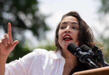 A woman passionately speaking at a rally with microphones in front of her