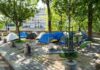 Tents set up in a city park surrounded by trees