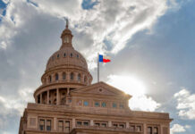 The Texas State Capitol building with a dome and the Texas flag flying under a cloudy sky