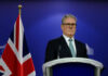 Brace for CHAOS: Labour’s Leadership on the Brink A political leader standing at a podium with a British flag in the background