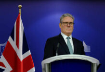 Brace for CHAOS: Labour’s Leadership on the Brink A political leader standing at a podium with a British flag in the background