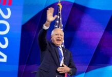 A man in a suit waving enthusiastically at an audience during a political event