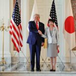 Two political leaders shaking hands in front of flags