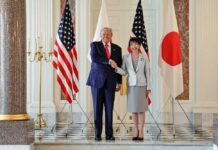 Two political leaders shaking hands in front of flags