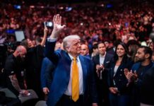 Trump’s Iran Strike HALTED – Two Weeks of Tension! A man in a blue suit with a yellow tie waves to a cheering crowd