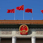 Chinese Spy Operation BUSTED — Mayor Forced Out Chinese flags and national emblem displayed on a government building against a blue sky