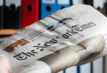 Newspaper held in hand with office binders in the background