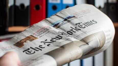 Newspaper held in hand with office binders in the background