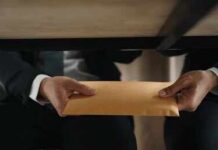 Six-Figure Bribes Rock NYC Government Hands passing a manila envelope under a table