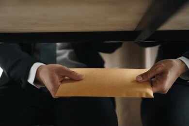 Hands passing a manila envelope under a table