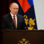 A government official delivering a speech at a podium with national flags in the background