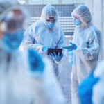Funding Bombshell Hits HIV Lifeline Healthcare workers in protective gear discussing information on a tablet outdoors