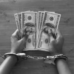 Medicare Heist Mastermind Nabbed Abroad Hands in handcuffs holding stacks of cash