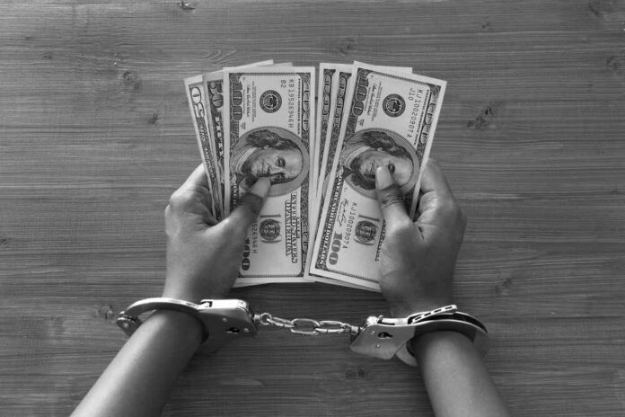 Hands in handcuffs holding stacks of cash