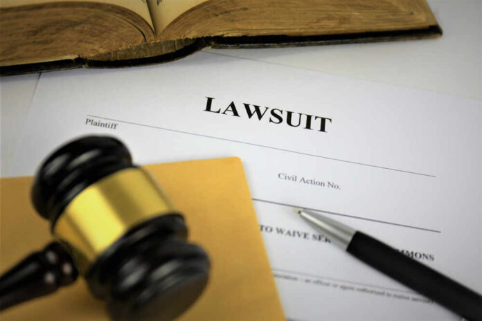 A gavel resting on a legal document titled 'LAWSUIT' with a pen and an open book in the background