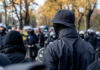 New York Mask Law Challenged A crowd of masked individuals facing law enforcement in an autumn setting