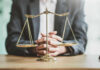 A lawyers hands resting on a table with a scale of justice in front