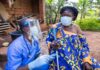 Global Health System Exposed—Ebola Chaos Deepens Healthcare worker in PPE talks with elderly woman using a crutch outdoors
