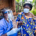 Global Health System Exposed—Ebola Chaos Deepens Healthcare worker in PPE talks with elderly woman using a crutch outdoors