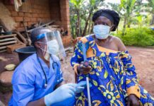 Healthcare worker in PPE talks with elderly woman using a crutch outdoors