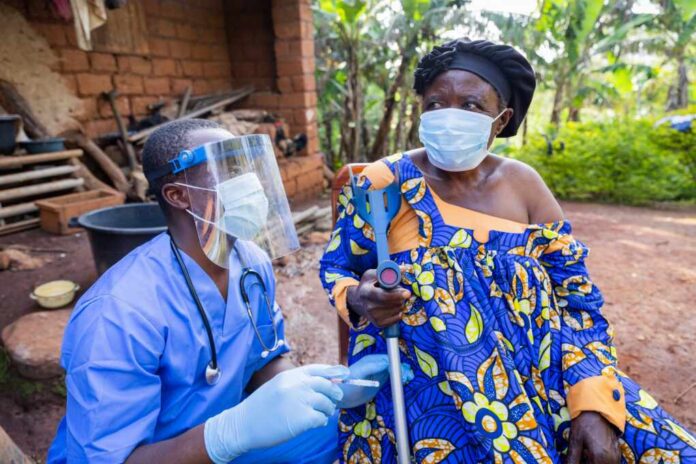 The,Village,Doctor,Visits,A,Sick,Old,Woman,And,Gives Healthcare worker in PPE talks with elderly woman using a crutch outdoors