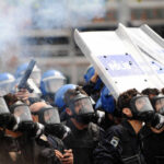 Encrypted J6 Cache Suddenly Resurfaces Riot police in gas masks with shields amid smoke