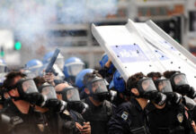 Riot police in gas masks with shields amid smoke