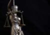 Lady Justice statue holding balanced scales against a dark background