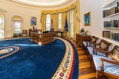 Oval office with wooden desk, blue rug, and gold curtains