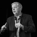 Man in a suit speaking into a handheld microphone