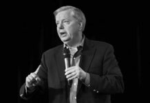 Graham’s Sudden Death Shocks Washington Man in a suit speaking into a handheld microphone