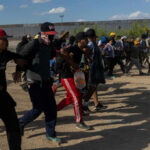 Defund Regret Rocks Democrats A group of migrants walking in a desert area towards a border