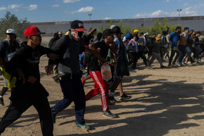 A group of migrants walking in a desert area towards a border