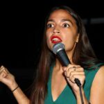AOC Targets Senate, Raises Eyebrows Again Woman speaking into a microphone on stage