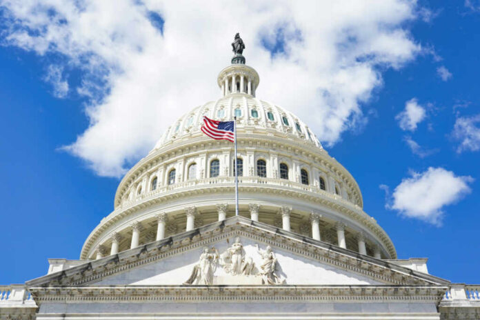 shutterstock_2465401345 The U.S. Capitol building with an American flag flying in front against a blue sky