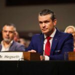 Hegseth Reverses Apache Pilot Suspension A man in a blue suit and red tie sitting at a hearing table with a nameplate