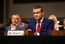 Hegseth Reverses Apache Pilot Suspension A man in a blue suit and red tie sitting at a hearing table with a nameplate
