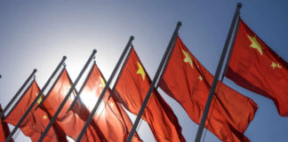 Multiple Chinese flags waving against a clear blue sky with sunlight in the background
