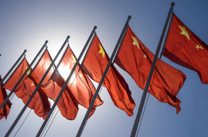 China,Flag Multiple Chinese flags waving against a clear blue sky with sunlight in the background