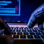 Terror Groups Move Recruitment Online Close-up of gloved hands typing on a laptop keyboard in a dark setting