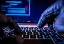 Terror Groups Move Recruitment Online Close-up of gloved hands typing on a laptop keyboard in a dark setting