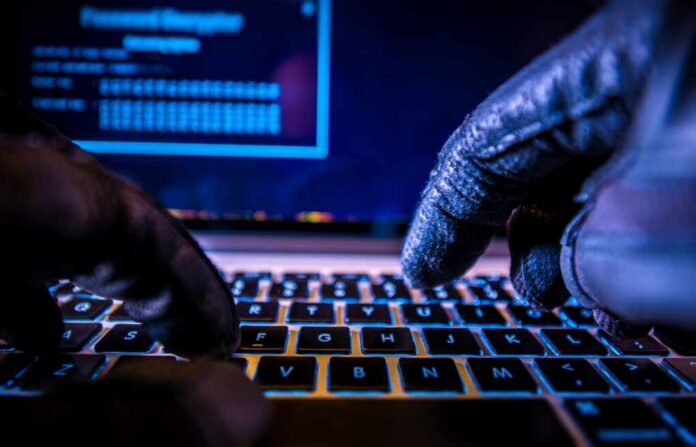Close-up of gloved hands typing on a laptop keyboard in a dark setting