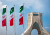 Tehran Mourners Target President Trump Three Iranian flags in front of the Azadi Tower against a blue sky