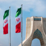 Tehran Mourners Target President Trump Three Iranian flags in front of the Azadi Tower against a blue sky