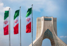 Tehran Mourners Target President Trump Three Iranian flags in front of the Azadi Tower against a blue sky