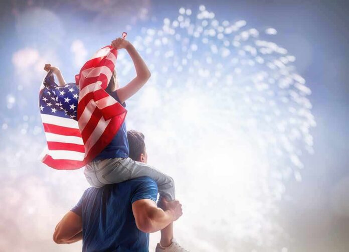 shutterstock_1099453688 Child on adult's shoulders holding American flag during fireworks