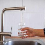 Hand filling a glass with water from a kitchen faucet