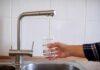 Hand filling a glass with water from a kitchen faucet