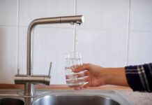 Silent Attack on America’s Faucets Hand filling a glass with water from a kitchen faucet